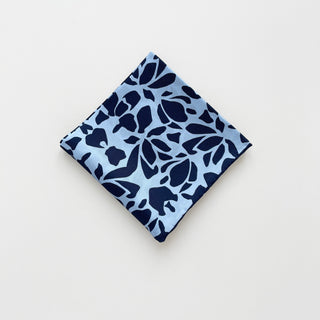 Folded Blue Melody Silk Scarf with navy abstract floral pattern on light blue background, featuring hand-rolled edges and square 65cm format