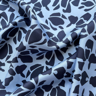 Luxurious silk scarf with abstract navy pattern on light blue background, showing soft draping and silky texture of the fabric