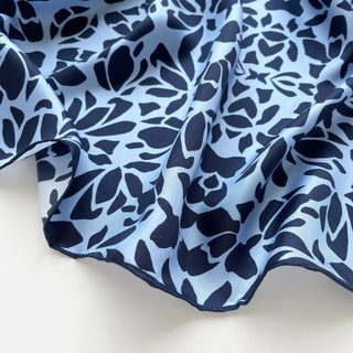 Luxury silk scarf with abstract navy pattern on light blue background, showing silky texture and hand-rolled edge detail