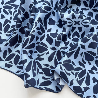 Luxury silk scarf with abstract navy pattern on light blue background, showing silky texture and hand-rolled edge detail