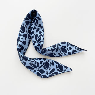 Light blue silk scarf with navy blue floral pattern, elegantly draped to showcase its smooth texture and hand-rolled edges against white background