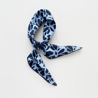 Blue Melody silk scarf with navy abstract pattern on light blue background, elegantly tied in a casual knot showing lustrous silk texture