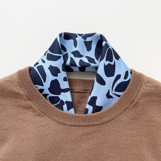 Blue Melody silk scarf with navy abstract pattern on light blue background, styled with a camel sweater showing elegant neckwear presentation