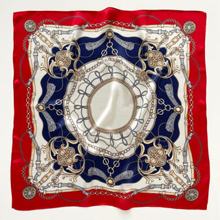 Square silk scarf with red border and navy center featuring ornate equestrian-inspired design with decorative chains, buckles, and floral elements in gold and silver tones.
