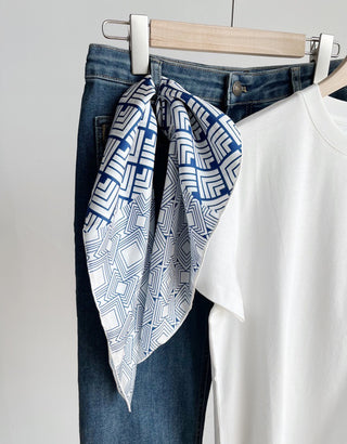 White silk bandana with blue geometric pattern styled on denim jeans hanging beside a white t-shirt, showcasing versatile fashion pairing