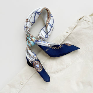 Turquoise & Navy Baroque Bridle silk scarf elegantly tied on a cream shirt, displaying equestrian pattern with ornamental chains and decorative elements