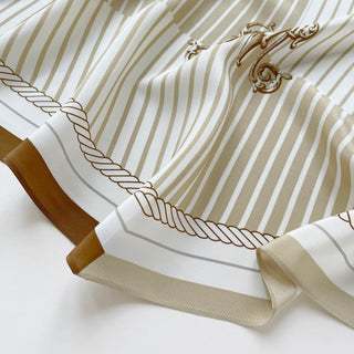 Elegant beige and white striped silk scarf with gold monogram accent and decorative rope design, featuring a luxurious cream border