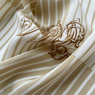 Close-up of beige and white striped silk scarf fabric with elegant brown monogram design, showcasing luxurious Crepe de Chine texture