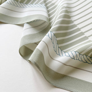 Luxurious silk scarf in sage green and beige with elegant striped pattern and decorative rope monogram, showing silky texture and flowing drape