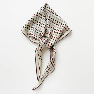 Ivory silk scarf with burgundy and navy geometric block pattern, elegantly folded with hand-rolled edges showcasing its luxurious twill texture