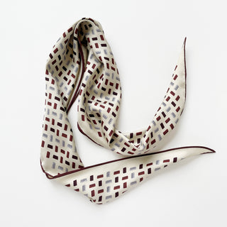 Long ivory silk scarf with geometric burgundy and navy block pattern, featuring hand-rolled edges and luxurious twill texture displayed in an elegant drape