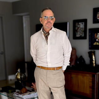 Men’s heritage geometric silk scarf in brown and beige tones styled with a linen shirt and pleated trousers; refined, classic look with warm neutrals.