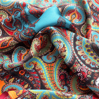 Close-up of turquoise silk scarf with vibrant paisley pattern in orange, red, and gold. Silky fabric shows intricate bohemian design with flowing folds.