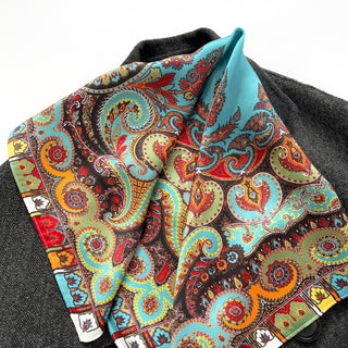 Turquoise silk square scarf with vibrant paisley pattern featuring orange, red, and green bohemian designs, displayed on dark fabric