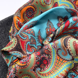 Silky turquoise scarf with vibrant bohemian paisley pattern in orange, red, and green. Luxurious texture shown in elegant folds.