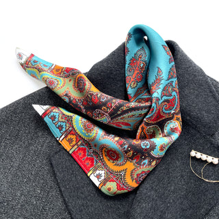 Turquoise and orange silk scarf with intricate bohemian paisley pattern, styled as a neckerchief on dark gray fabric with pearl accessory