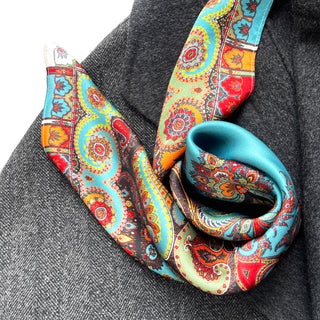 Vibrant turquoise and orange silk scarf with intricate bohemian paisley patterns draped elegantly over a gray coat, showcasing its luxurious sheen and colorful design.