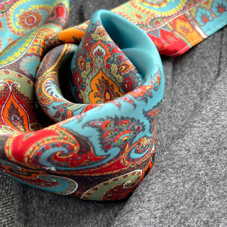 Close-up of luxurious turquoise and orange silk scarf with intricate bohemian paisley pattern, elegantly draped on gray background