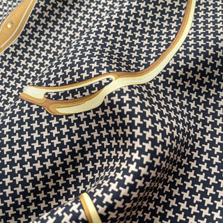 Close-up of luxury silk scarf with black and beige houndstooth pattern and gold equestrian-inspired border detail, showing fine twill texture