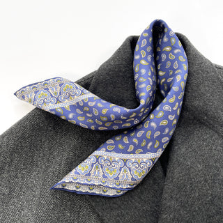 Blue silk neckerchief with paisley pattern and decorative border, elegantly draped over a gray wool coat, showcasing its luxurious texture and vibrant design