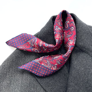 Plum red silk neckerchief with classic paisley pattern and navy blue borders featuring small floral details, elegantly styled on a gray coat.