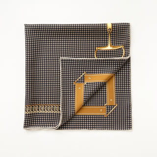 Folded black and beige houndstooth silk scarf with hand-rolled edges, featuring gold equestrian accents and decorative border on a 65cm square twill fabric