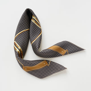 Elegant black and beige silk scarf with classic houndstooth pattern, gold accents, and hand-rolled edges, displayed in a graceful S-shape against white background.