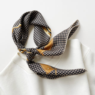 Luxury 65cm silk scarf with black and beige houndstooth pattern, gold equestrian accent border, styled in a knot on white fabric