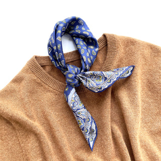 Blue silk neckerchief with paisley pattern tied around collar of camel sweater, showcasing hand-rolled edges and luxurious twill fabric