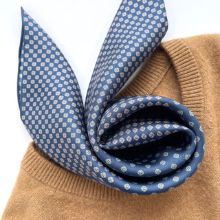 Blue silk neckerchief with white four-leaf clover pattern elegantly draped over camel-colored sweater, showcasing luxurious texture and hand-rolled edges