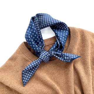 Blue silk neckerchief with four-leaf clover pattern tied stylishly around camel sweater collar, showcasing luxurious hand-rolled edges