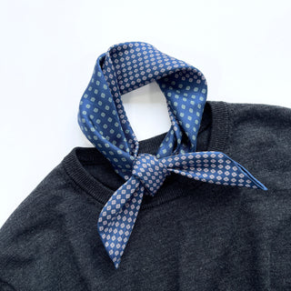 Blue silk neckerchief with four-leaf clover pattern elegantly tied around collar of dark gray sweater, showcasing luxurious texture and styling