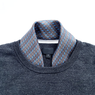 Charcoal grey silk neckerchief with light blue geometric pattern draped inside collar of dark grey sweater, showcasing luxurious texture