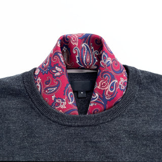 Plum red silk neckerchief with navy blue paisley pattern styled with a dark gray sweater, showcasing elegant hand-rolled edges