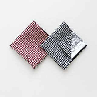 Two luxury silk scarves with houndstooth pattern - one in deep red and white, one in black and white, folded to display hand-rolled edges and fabric texture