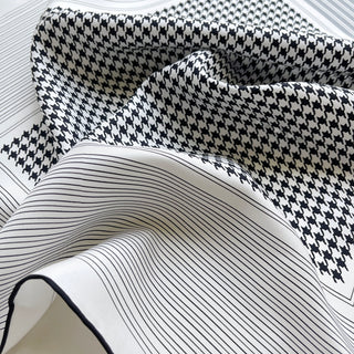 Elegant silk scarf with classic black and white houndstooth pattern bordered by fine pinstripes, showcasing luxurious fabric texture and hand-rolled edges