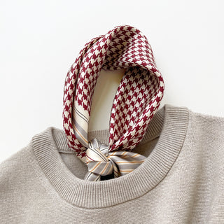 Red and cream houndstooth silk scarf elegantly tied around the neck of a beige sweater, displaying luxurious texture and classic pattern