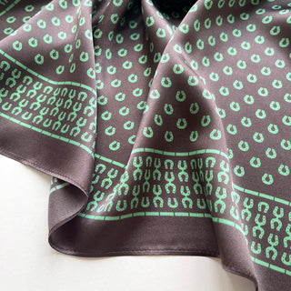 Silk scarf in brown with mint green horseshoe pattern, featuring decorative border and elegantly draped to showcase the smooth satin texture.
