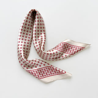 Beige silk scarf with red horseshoe pattern, elegantly draped to showcase its lustrous satin finish and distinctive border design.
