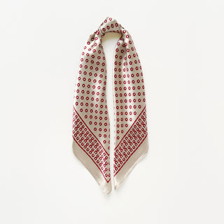 Beige silk scarf with red horseshoe pattern throughout and decorative border, displayed draped in a triangle shape against white background