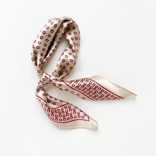 Silk scarf with beige background and red horseshoe pattern, elegantly tied to showcase its smooth satin texture and 65cm square design