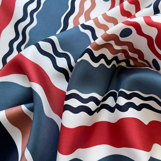 Silk twill scarf with flowing wave pattern in navy blue, red, and earthy tones, showing the luxurious fabric texture with hand-rolled edges
