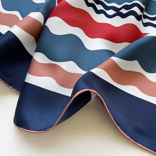 Blue Wave silk scarf with wavy pattern in navy, red, and earthy tones, featuring hand-rolled edges and smooth twill texture
