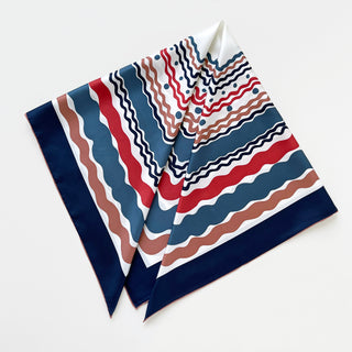Square silk scarf with wave pattern in navy blue, red, and earthy brown on white background, featuring hand-rolled edges and elegant navy border