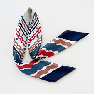 Elegant silk scarf with wavy pattern in navy, red, and terracotta tones on white background, displaying hand-rolled edges and luxurious twill texture