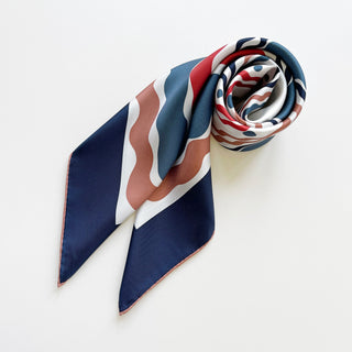 Blue Wave silk scarf with hand-rolled edges displayed on white background, featuring navy, red, and coral wave pattern in elegant 90cm twill design