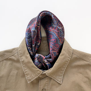 Navy blue silk neckerchief with intricate burgundy paisley pattern styled on beige shirt collar, showcasing luxurious sheen and bohemian design