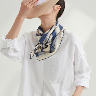 Luxury silk scarf with blue and cream striped pattern, styled with hand-rolled edges, worn with white linen shirt and straw hat for elegant summer look