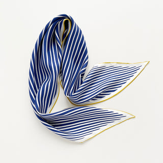 Triangle silk scarf with deep blue and white diagonal stripes, featuring elegant yellow hand-rolled edges, displayed in a flowing arrangement on white background.