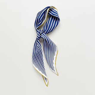 Triangle silk scarf with navy blue and white stripes, elegantly tied with gold trim edges, displayed on light background